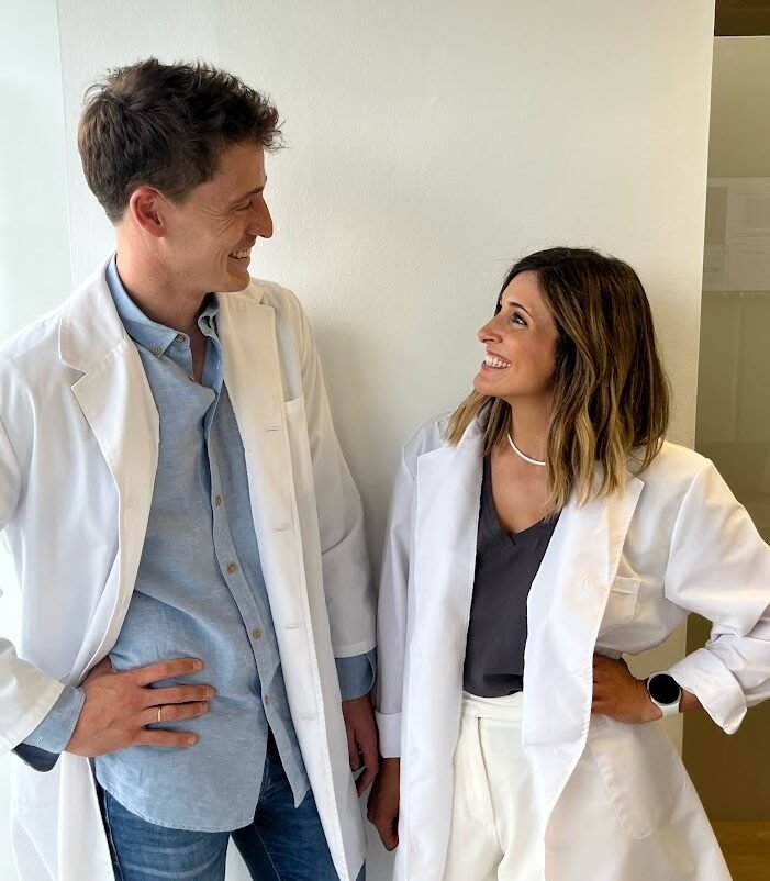 Alejandro y Laura, dietistas-nutricionistas de la clínica Nubamind en Carabanchel, mirándose y sonriendo con bata blanca en su consulta.